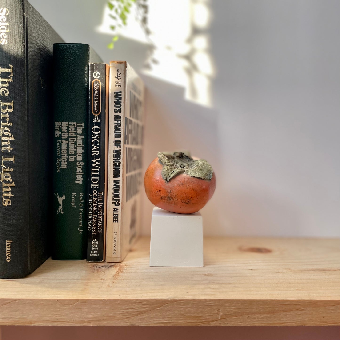 Persimmon made of plaster and hand painted fake fruit styled on a bookshelf 